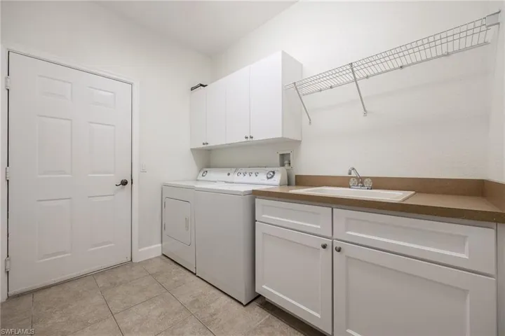 Laundry area with sink, cabinets, washer and dryer, and light tile patterned floors