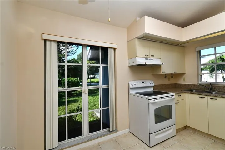 Kitchen featuring white range with electric stovetop, under cabinet range hood, dark countertops, light tile patterned floors, and cream cabinetry