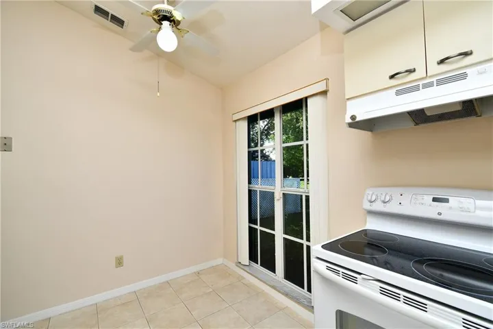 Kitchen with white range with electric cooktop, under cabinet range hood, light tile patterned flooring, and ceiling fan