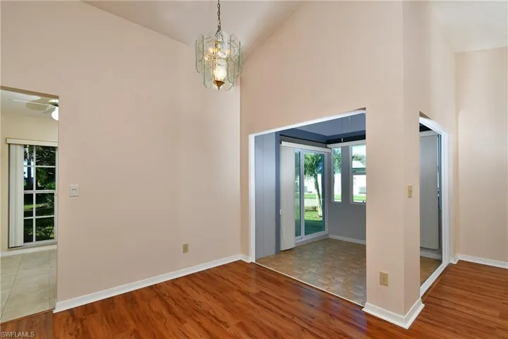 Empty room featuring high vaulted ceiling, healthy amount of natural light, wood finished floors, a chandelier, and a ceiling fan