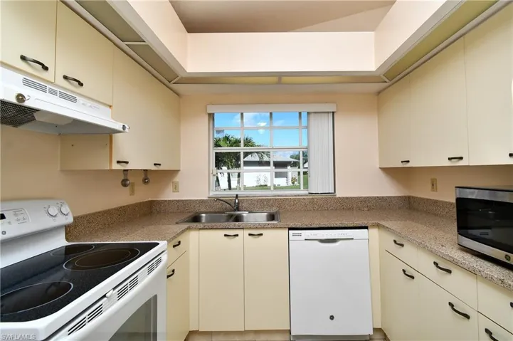 Kitchen featuring white appliances, under cabinet range hood, light countertops, and cream cabinets