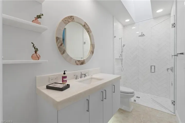 Herringbone Carrara marble in shower with Kohler rainforest shower-head and body sprays. Carrara marble shelving alongside Cabico vanity with quartzite countertop.