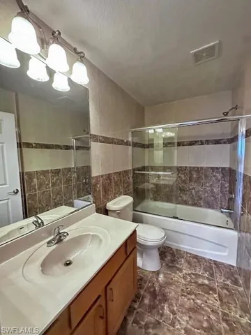 Full bath with vanity, enclosed tub / shower combo, tile walls, and a textured ceiling