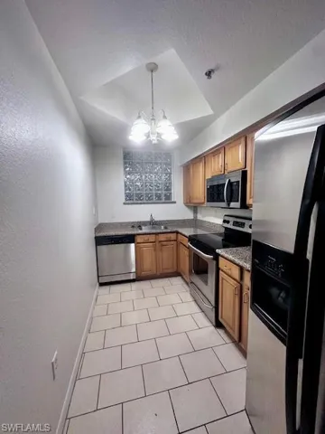 Kitchen with wood finish cabinetry, stainless steel appliances, hanging lights, dark stone counters, and a textured wall