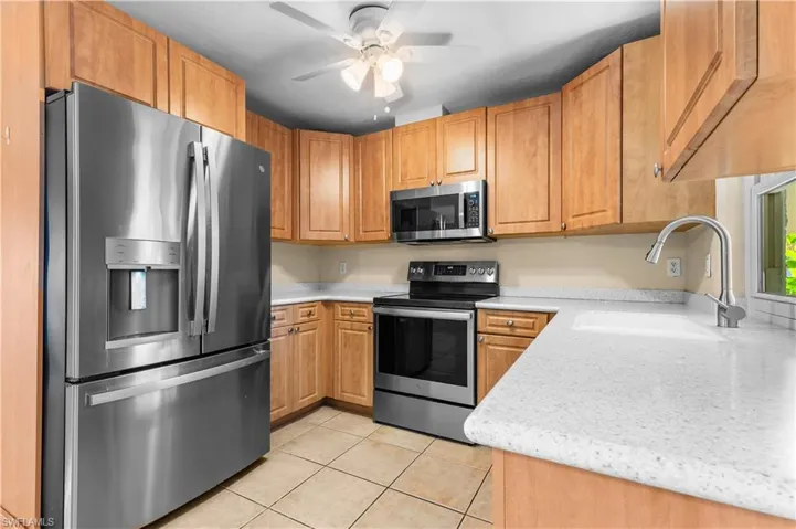 Kitchen with appliances with stainless steel finishes, light stone counters, light tile patterned floors, a ceiling fan, and brown cabinetry
