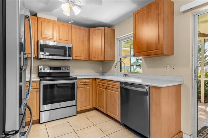 Kitchen featuring appliances with stainless steel finishes, a ceiling fan, light tile patterned flooring, and brown cabinetry