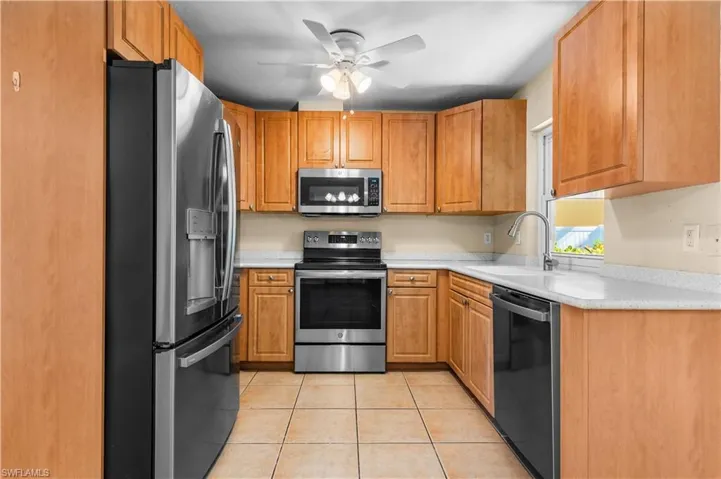 Kitchen with stainless steel appliances, light tile patterned floors, a ceiling fan, and brown cabinetry