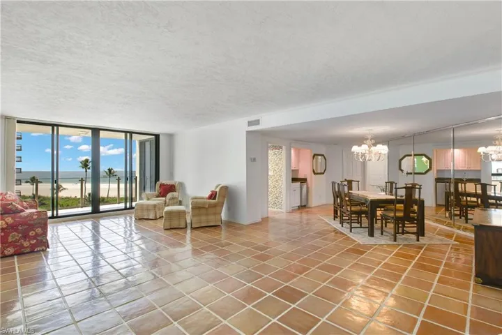 Living area featuring view of water and beach, a textured ceiling, expansive windows, light tile patterned floors, and a chandelier