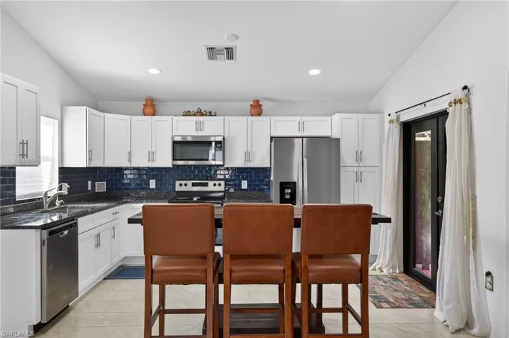 Kitchen with lofted ceiling, white cabinetry, stainless steel appliances, dark stone counters, and light tile patterned floors