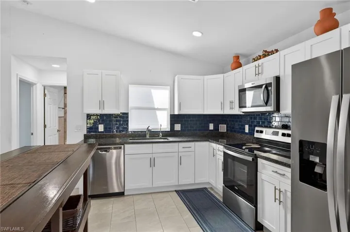 Kitchen featuring stainless steel appliances, white cabinets, lofted ceiling, dark stone countertops, and tasteful backsplash
