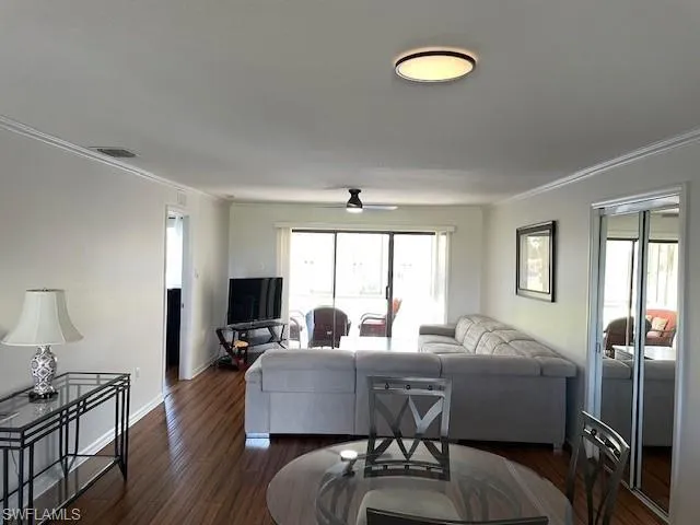 Living area featuring ornamental molding, dark wood finished floors, and a ceiling fan