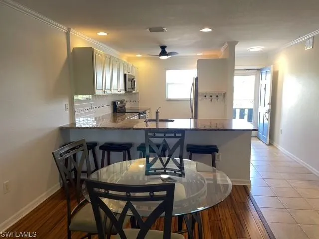 Kitchen with a breakfast bar, appliances with stainless steel finishes, dark wood finished floors, a peninsula, and ornamental molding
