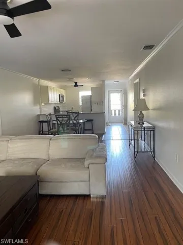 Living area featuring crown molding, dark wood-style flooring, a ceiling fan, and a textured wall