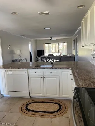 Kitchen with stove, white cabinets, dishwashing machine, open floor plan, and dark stone countertops