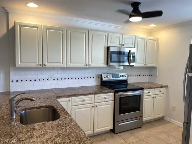 Kitchen featuring appliances with stainless steel finishes, backsplash, ceiling fan, crown molding, and dark stone counters