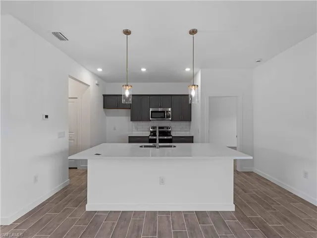 Kitchen with appliances with stainless steel finishes, baseboards, dark wood finished floors, and recessed lighting