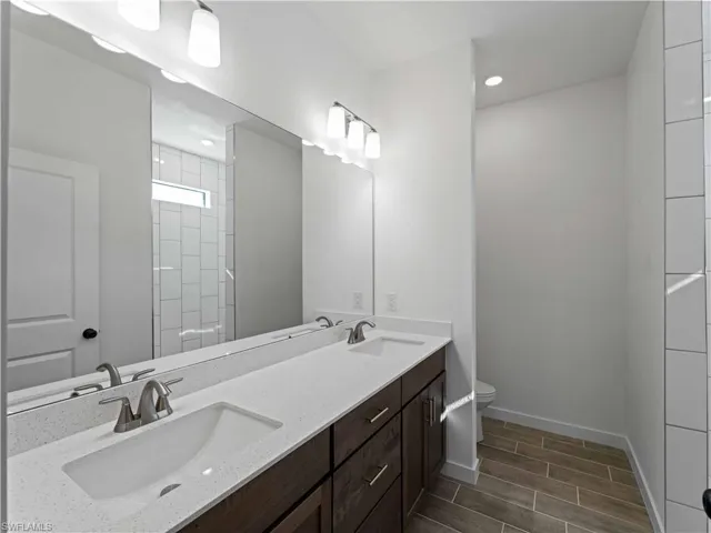 Bathroom with toilet, wood tiled floors, baseboards, double vanity, and a shower