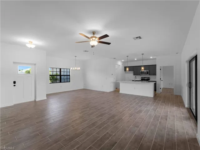 Unfurnished living room featuring ceiling fan, baseboards, dark wood-style flooring, a chandelier, and recessed lighting