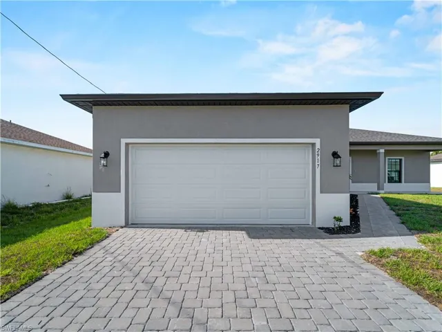 View of front facade featuring stucco siding, decorative driveway, and an attached garage