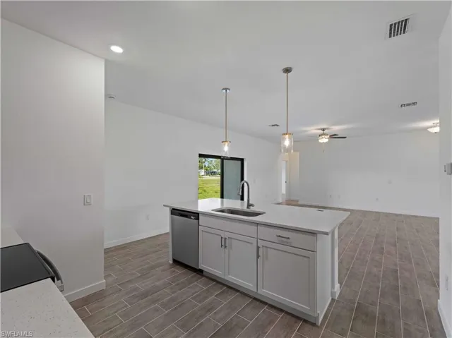 Kitchen featuring dishwasher, a sink, wood finish floors, light countertops, and baseboards