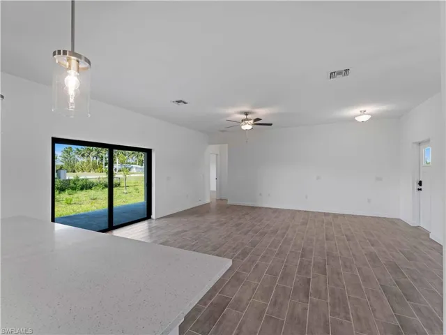Unfurnished living room featuring plenty of natural light, ceiling fan, dark wood-type flooring, and baseboards