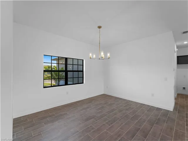 Spare room with a chandelier, baseboards, and dark wood-type flooring