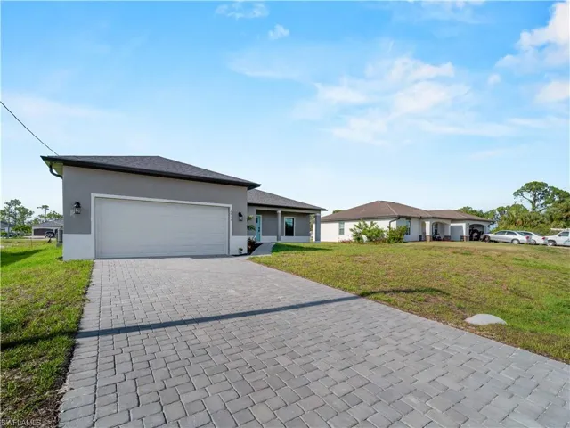 Ranch-style home featuring a front lawn, decorative driveway, stucco siding, and a garage