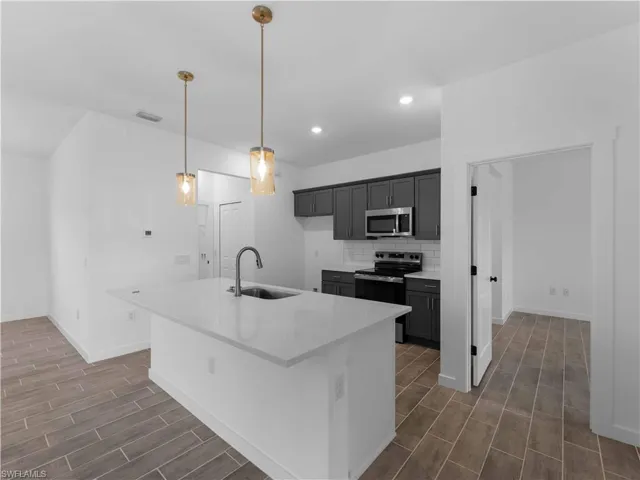 Kitchen featuring a sink, appliances with stainless steel finishes, wood finish floors, baseboards, and tasteful backsplash