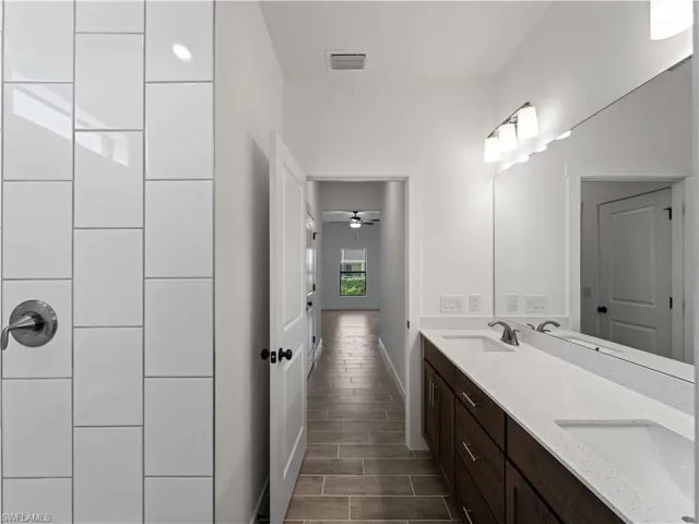 Full bath with double vanity, wood finish floors, baseboards, and a ceiling fan