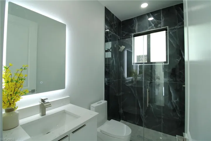 Bathroom with a shower with shower door, vanity, and toilet
