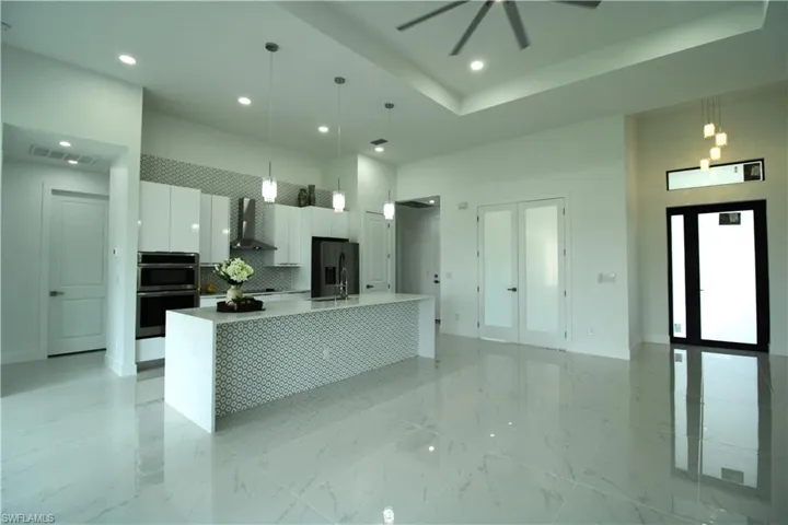 Kitchen featuring wall chimney range hood, pendant lighting, stainless steel appliances, and white cabinetry