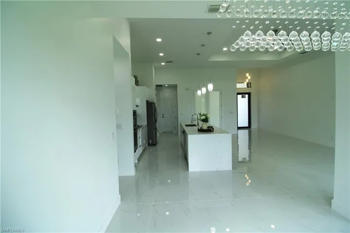 Kitchen with light tile flooring, black fridge, a raised ceiling, a towering ceiling, and sink