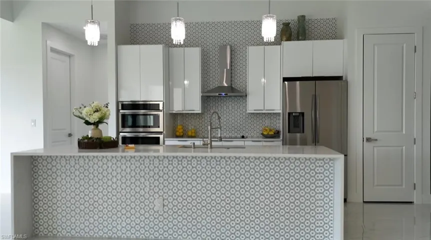 Kitchen with wall chimney range hood, stainless steel appliances, backsplash, sink, and pendant lighting