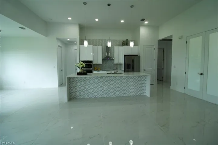 Kitchen featuring wall chimney range hood, white cabinets, light tile floors, and appliances with stainless steel finishes