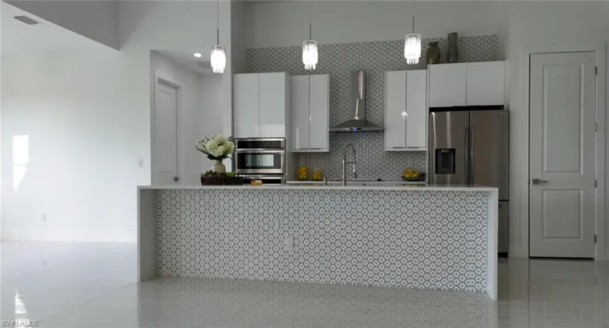Kitchen with decorative light fixtures, wall chimney range hood, light tile flooring, tasteful backsplash, and appliances with stainless steel finishes