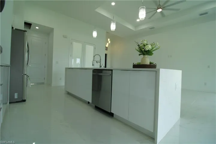 Kitchen with a tray ceiling, stainless steel appliances, a center island with sink, light tile flooring, and pendant lighting