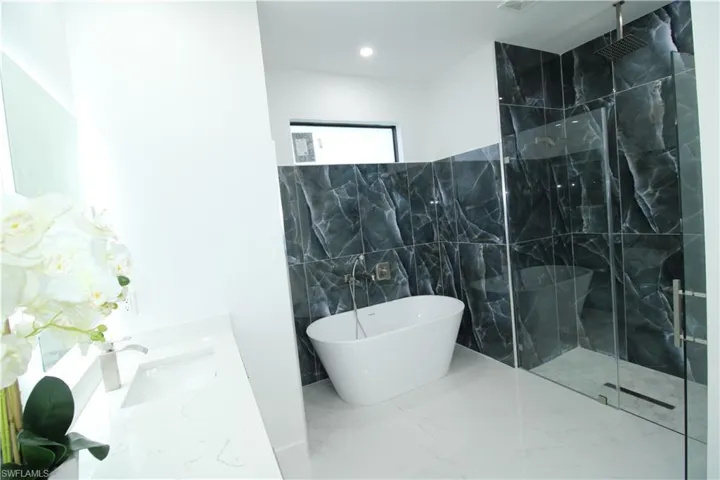 Bathroom featuring tile flooring, shower with separate bathtub, sink, and tile walls