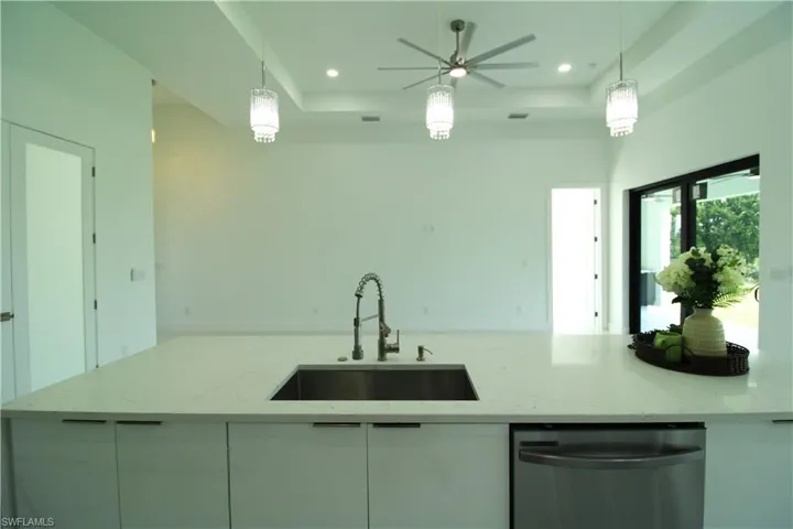 Kitchen featuring decorative light fixtures, light stone counters, ceiling fan, stainless steel dishwasher, and sink