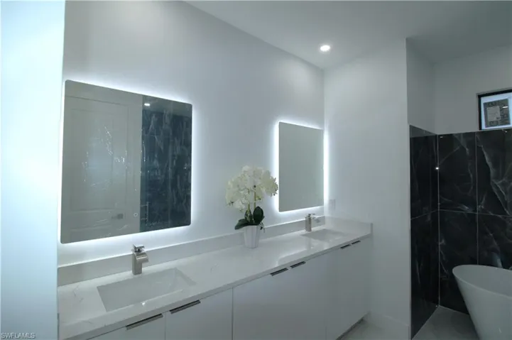 Bathroom featuring tile walls, a washtub, and dual bowl vanity