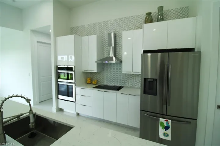 Kitchen with appliances with stainless steel finishes, white cabinets, wall chimney exhaust hood, sink, and tasteful backsplash
