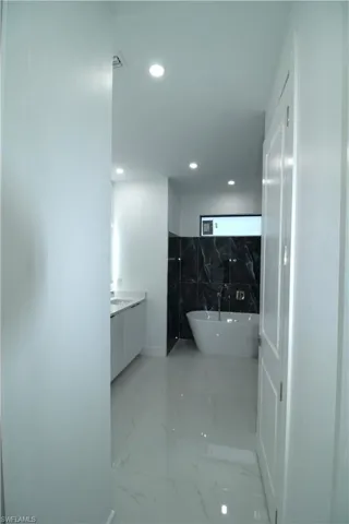 Bathroom with a washtub, tile flooring, vanity, and tile walls