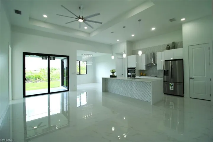 Kitchen with stainless steel fridge with ice dispenser, a raised ceiling, white cabinetry, wall chimney exhaust hood, and light tile floors