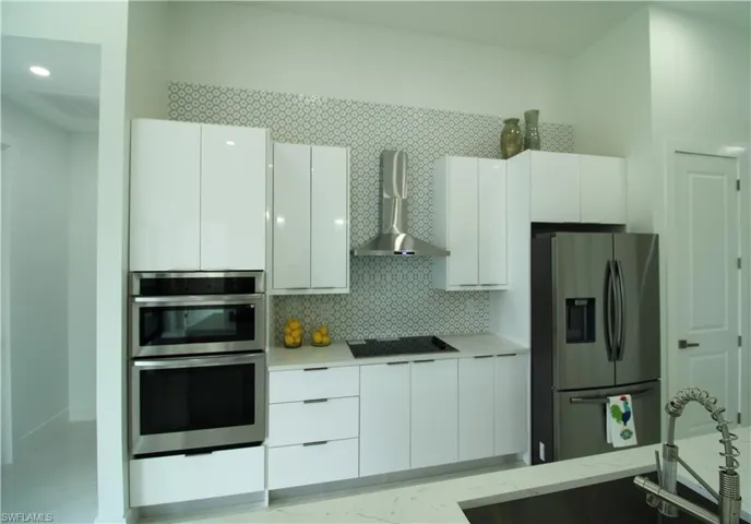 Kitchen with backsplash, wall chimney range hood, white cabinetry, and appliances with stainless steel finishes