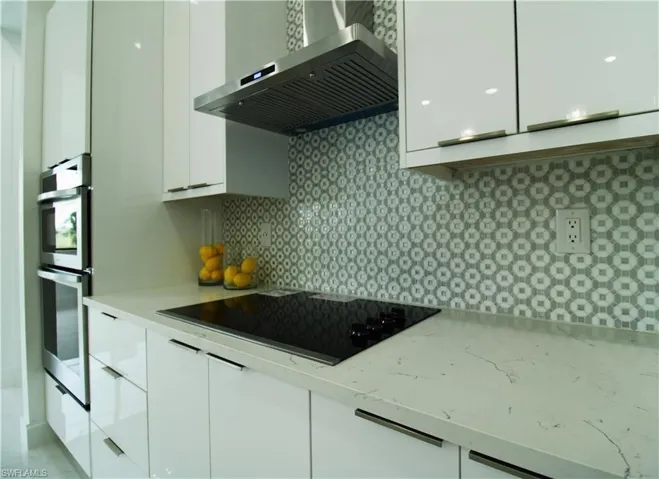 Kitchen featuring double oven, white cabinets, black electric cooktop, and wall chimney exhaust hood