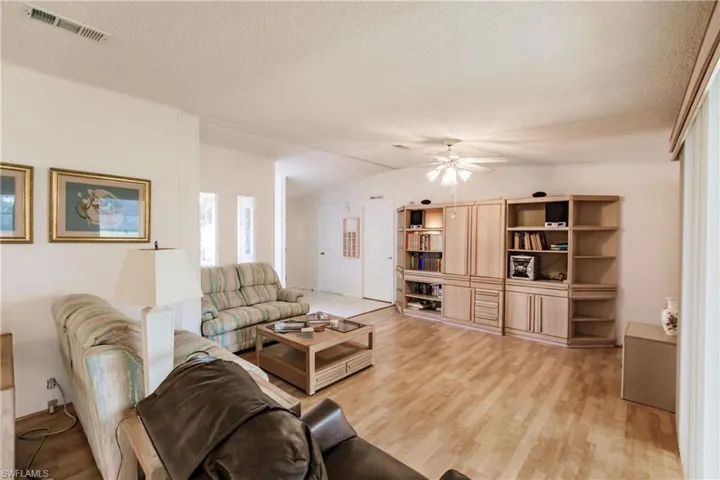 Living room with a textured ceiling, ceiling fan, light wood-type flooring, and vaulted ceiling