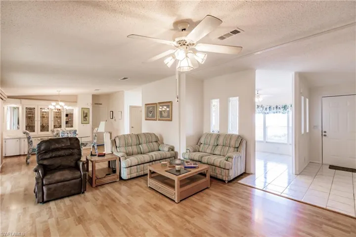 Living room with a textured ceiling, ceiling fan with notable chandelier, and light hardwood / wood-style floors