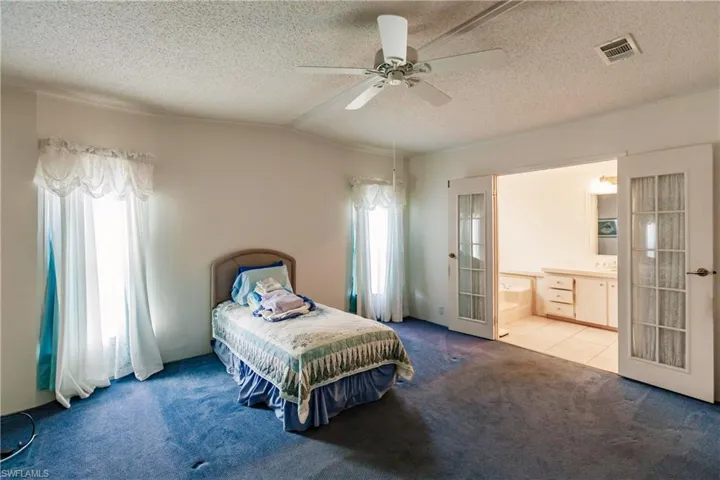 Bedroom featuring ensuite bath, ceiling fan, french doors, lofted ceiling, and carpet floors