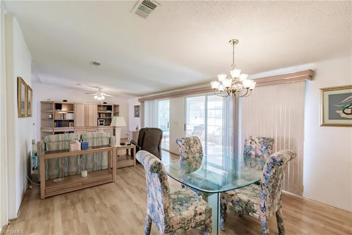 Dining space with ceiling fan with notable chandelier, a textured ceiling, and light hardwood / wood-style floors