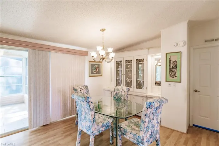 Dining area featuring a textured ceiling, an inviting chandelier, light hardwood / wood-style floors, ornamental molding, and lofted ceiling