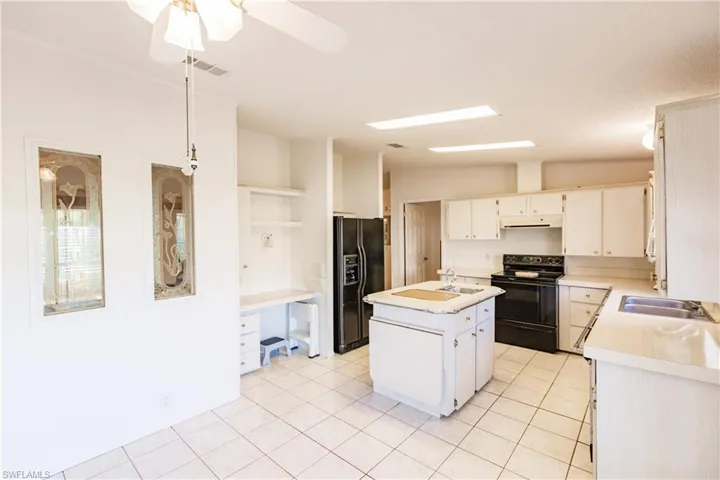 Kitchen with white cabinets, light tile patterned floors, black appliances, ceiling fan, and a center island with sink